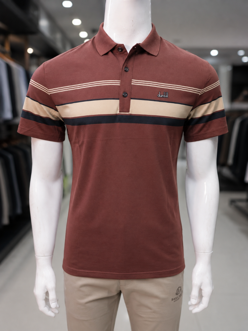 A short-sleeve polo shirt displayed on a white mannequin torso in a retail store. The shirt is rust brown with horizontal stripes in beige and black across the chest and sleeves.
