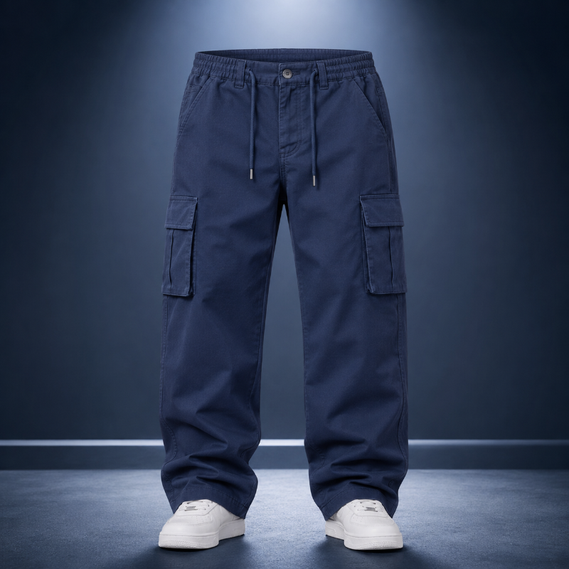 A pair of navy blue cargo pants with an elastic waistband, drawstring, and side cargo pockets, shown on a model from the waist down wearing white sneakers against a dark blue studio background.