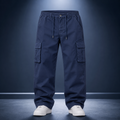 A pair of navy blue cargo pants with an elastic waistband, drawstring, and side cargo pockets, shown on a model from the waist down wearing white sneakers against a dark blue studio background.