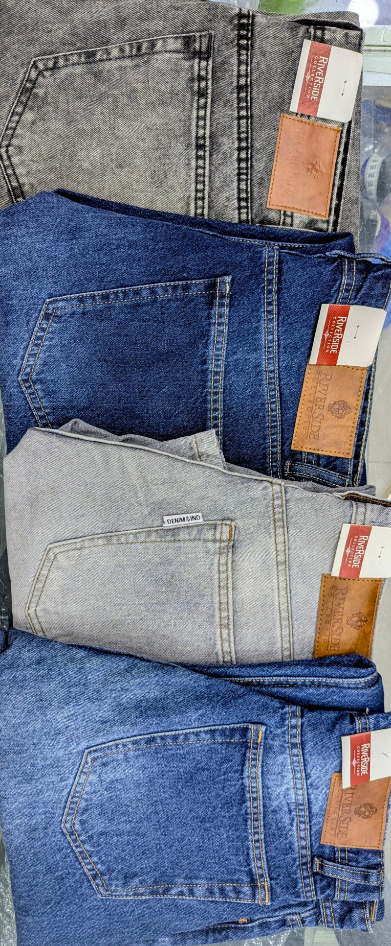 Four Colours of folded Baggy denim jeans in different washes stacked on top of each other, showing the back pockets and brown leather brand patches with white labels.