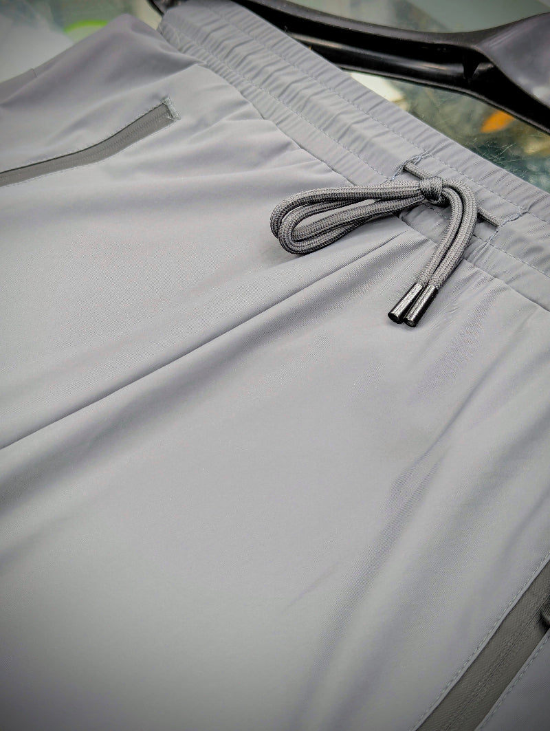 Close-up of light gray shorts showing the elastic waistband, drawstring, and side pocket details.