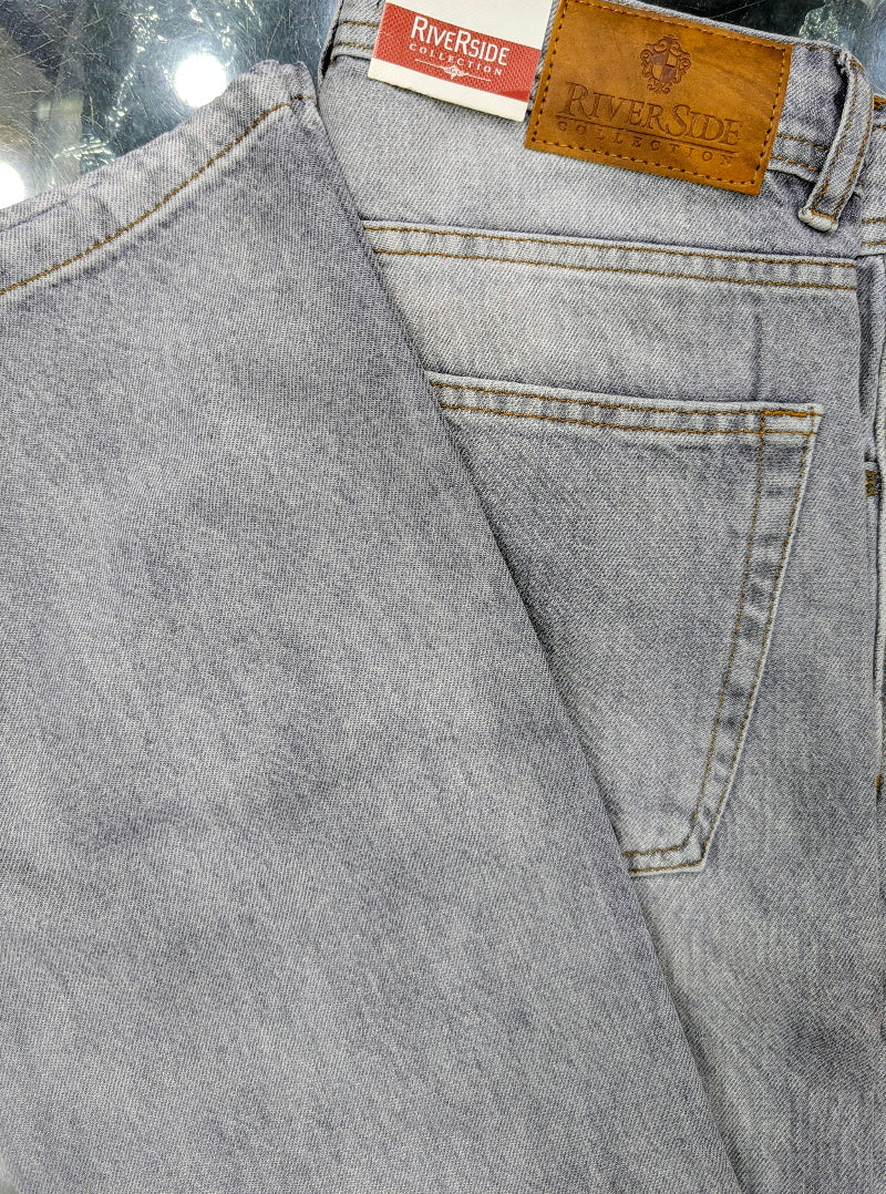 Close-up of folded light gray denim Baggy jeans showing the back pocket, waistband, and leather brand patches. The patches read Riverside.